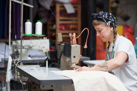 Young tattooed seamstress sewing in a factory environmentの写真素材