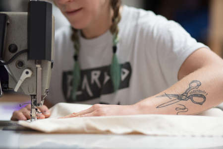 Young tattooed seamstress sewing in a factory environmentの写真素材