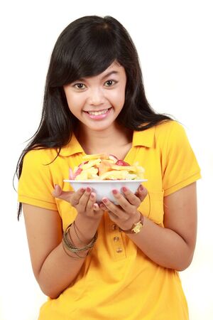 portrait of a smiling teenage girl holding a bowl of cut fruits against whiteの写真素材