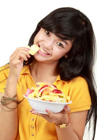 Closeup portrait of a smiling teenager eating a bowl of cut fruits against whiteの写真素材