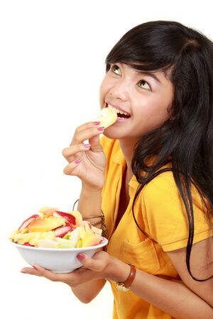 healthy young girl holding a bowl of sliced fruits while eatingの写真素材