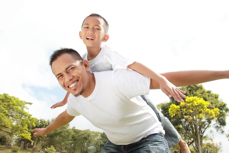 Portrait of father giving his son piggyback ride against skyの写真素材