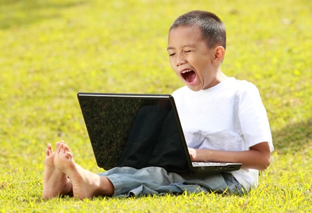 little boy yawning when playing laptop on the grassの写真素材