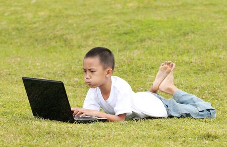 little boy playing laptop on the grassの写真素材