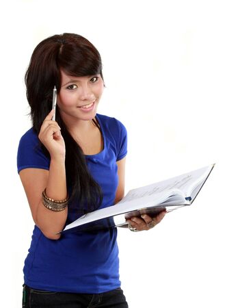 Pretty young woman thinking, holding pen and a notebook textbook in her hands on a white background.の写真素材