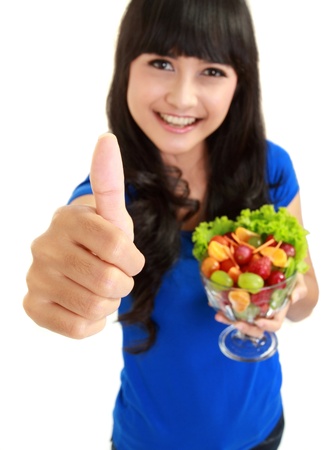 Portrait of a smiling woman with a bowl of fruit salad wishing you luck in isolated backgroundの写真素材