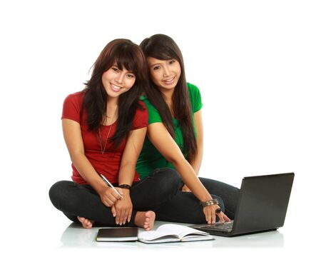Two girls-students with laptop sitting on white backgroundの写真素材