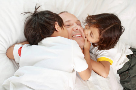 son kissing their father on the bed