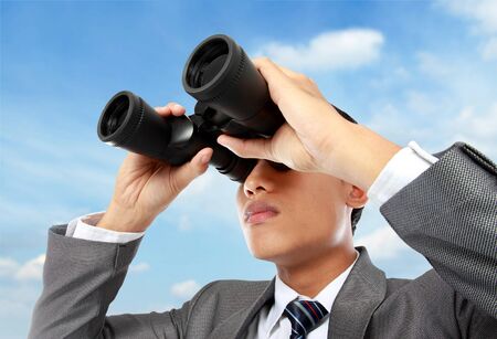 Closeup of a young business man looking through binocular in blue skyの写真素材