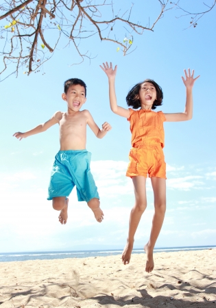 Portrait of happy asian kids in the beach jumping togetherの写真素材