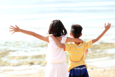 Cute little girl and boy raises their hands against blue skyの写真素材