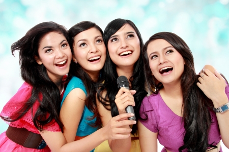 Four beautiful young woman singing karaoke togetherの写真素材