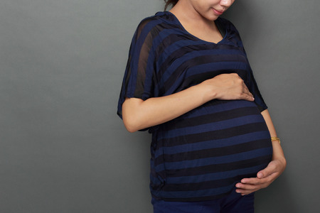 Pregnant Woman holding her belly on Grey Backgroundの写真素材