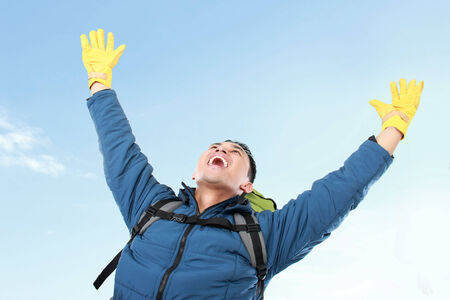 portrait of male hiker with backpack raised his arm under the blue skyの写真素材