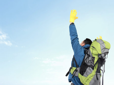 portrait of male hiker with backpack raised his arm. shoot from behind under the blue skyの写真素材
