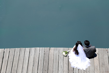 top view portrait of bride and groom sitting on the edge of the river bridge with copy spaceの写真素材