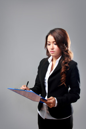 A portrait of a young businesswoman writing on a clipboard while thinkingの写真素材