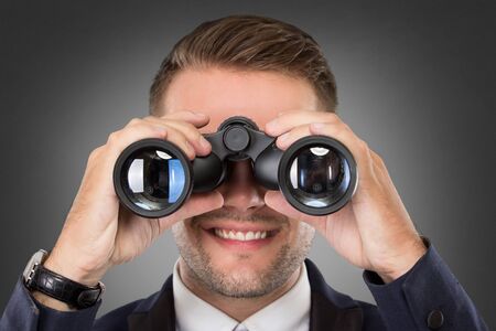 A portrait of a young businessman looking through binoculars - market research conceptの写真素材