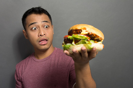 A portrait of a young man surprised with the size of his burgerの写真素材