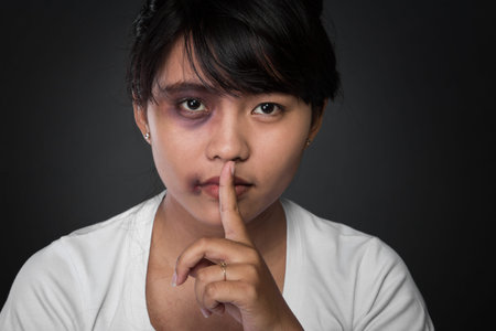 A portrait of close up of an asian girl. Holding her finger, showing to keep silent.