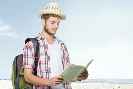 portrait of a young traveling man with backpack looking for and reading mapの写真素材