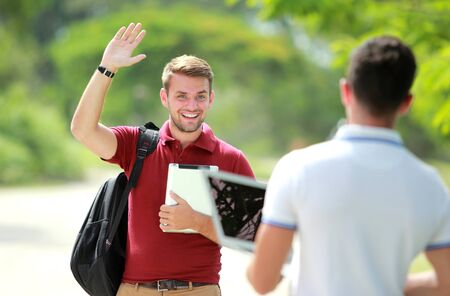 portrait of handsome college student happy to meet his friend and waving his handの写真素材
