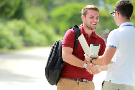 portrait of a college student with backpack happy to meet his friend and then shake hands with copy spaceの写真素材