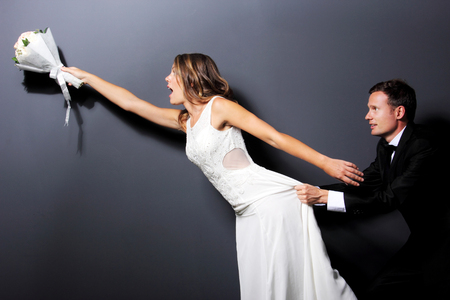 portrait of bride and groom trying to catch a bouquet with dark backgroundの写真素材