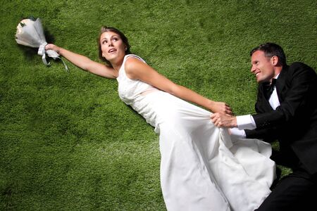 portrait of bride and groom trying to catch a bouquet with grass backgroundの写真素材