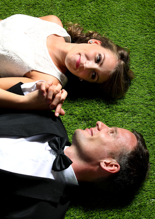 portrait of bride and groom lying on the grass while holding each other handsの写真素材