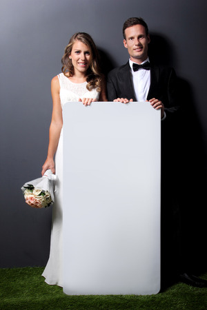 full length portrait of  young newlywed couple holding white boardの写真素材