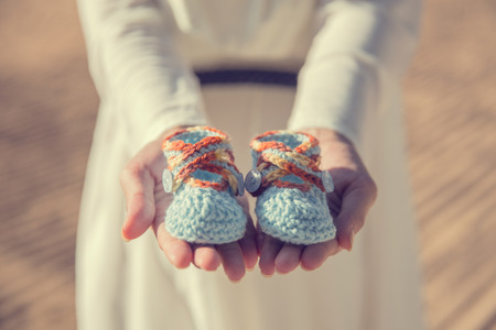 close up portrait of woman hands holding a pair of baby shoesの写真素材