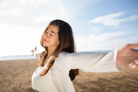 A portrait of an Asian woman enjoying her time in the beach, closing her eyes and arms open wideの写真素材