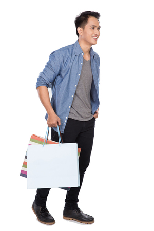 A portrait of young asian man walking and holding shopping bags, full bodyの写真素材