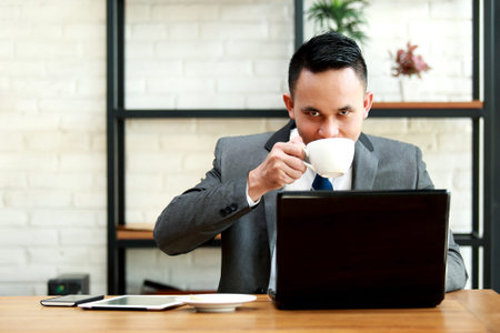 young businessman drinking a coffee while working on laptop at office