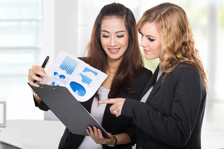 A portrait of a two young businesswoman wtih a clipboard discussingの写真素材