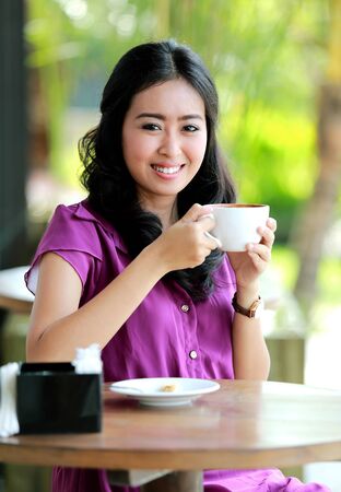 portrait of beautiful woman smiling while holding a cup of coffee at cafeの写真素材