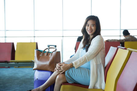 Woman in the aiport lounge sitting in chair by the window waiting for her schedule to flyの写真素材