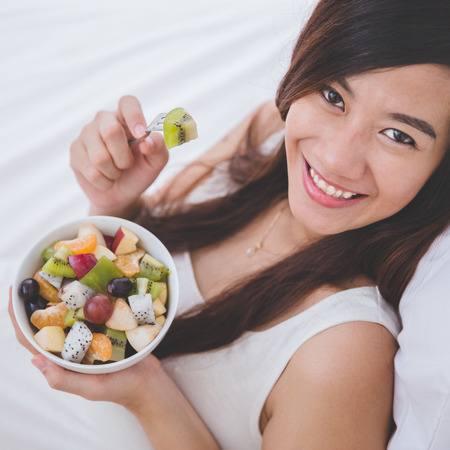 A portrait of a Beautiful pregnant woman with a bowl of fruit, ready to eatの写真素材