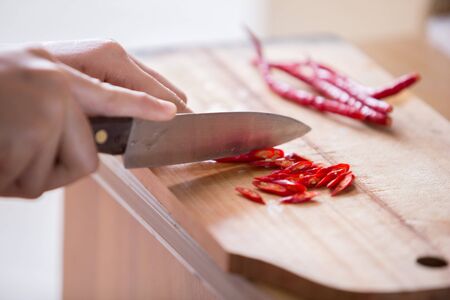 Hand slicing Chilli pepper with Knife on chopping board on wooden background.の写真素材