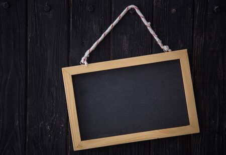 A portrait of a black chalkboard hanging on dark wooden background, horizontally placedの写真素材