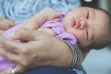 A portrait of newborn baby curled up in  arms, close up