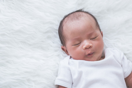 A portrait of asian newborn baby sleeping peacefully on the furry bedの写真素材