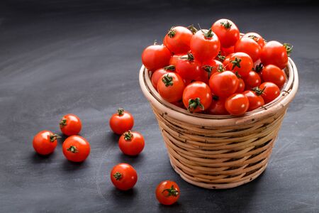 full view portrait of pile of cherry tomatoes in a rattan basket on black board for backgroundの写真素材