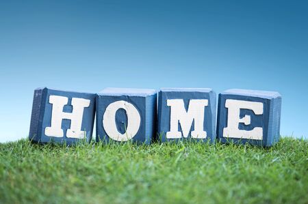 still life of HOME sign concept made of wooden blocks on a green grass under the bright blue skyの写真素材