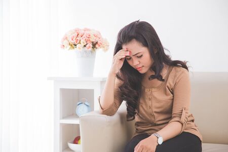 Woman sitting in a couch while touching her forehead. feeling depressedの写真素材
