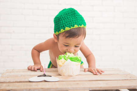 A portrait of a Cute caucasian boy wearing a green knit hat with a bread in front of himの写真素材