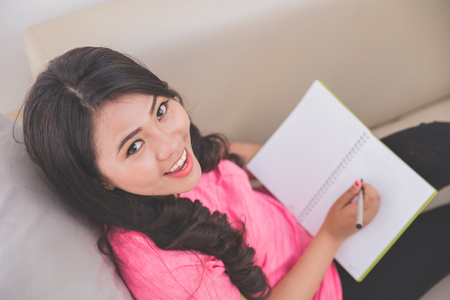 Woman holding notebook sitting on a couch, writing, looking upの写真素材