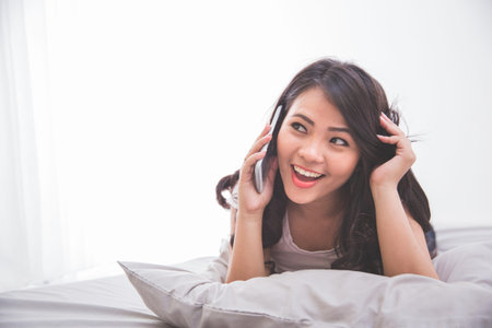 Woman speaking on the phone while laying on the  bedの写真素材