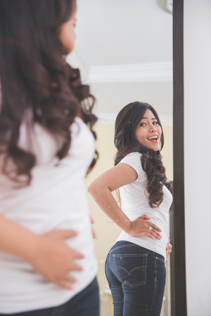 Woman looking her image on the mirror, happy to see her slim figureの写真素材